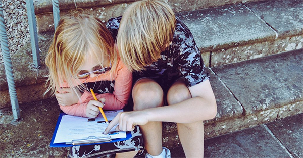 Two children sitting on some steps and looking at a workbook.