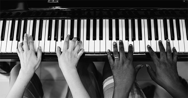 Two sets of hands on a piano keyboard.