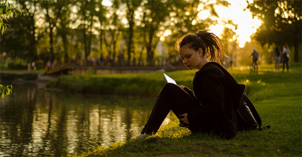 A person sitting outside by water and trees.