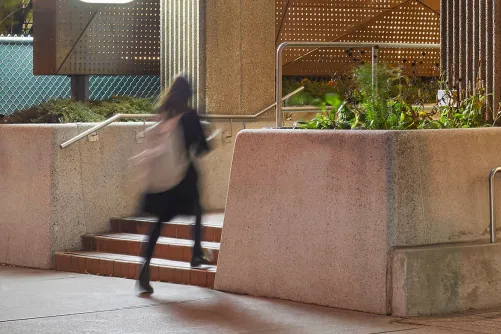 A student walking up stairs outside the OISE building at night.