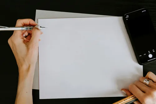 A person writing on a white paper, with a phone on the right.