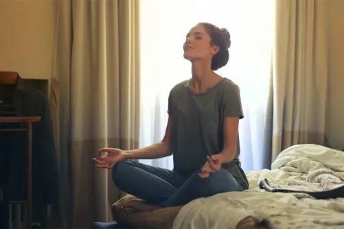 A person meditating on a bed.