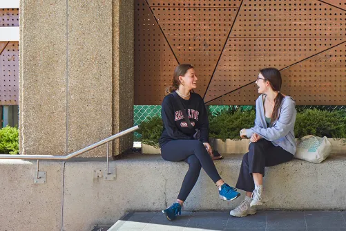 Two students sitting outside the OISE Building.