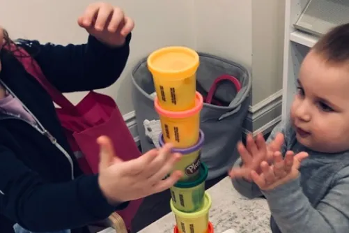 Two children stacking containers of Play-Doh. 