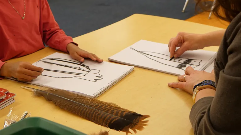 A JICS student and teacher drawing a feather.