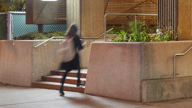 A student walking up stairs outside the OISE building at night.