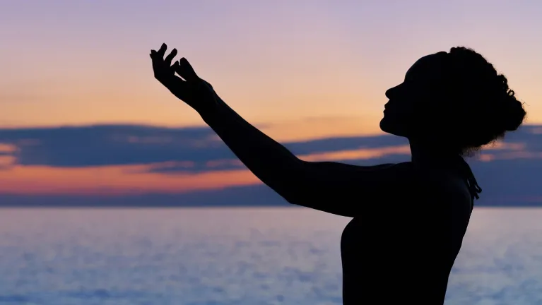 A silhouette of a person mediating outside on a beach.