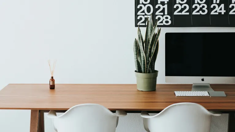 A workspace with two chairs, a desk, a plant and a calendar in the background.