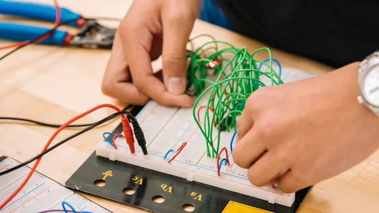 A person working on a circuit board on a desk with multiple cables/wires.