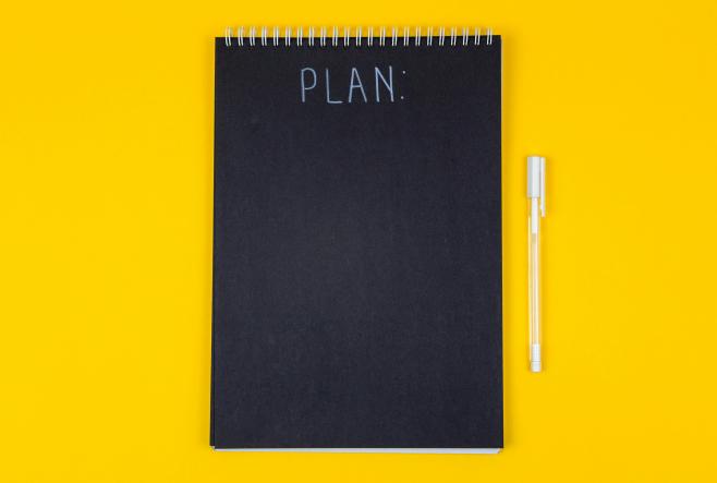 Image depicting a black notebook with the word "Plan" written on top of it.