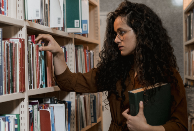 Female student looking for a book on a library shelf.